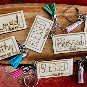 May include: Wooden keyrings with tassels in various colours. Each keyring features a different inspirational word, such as "Blessed", "Loved", and "Worthy", with a corresponding Bible verse.