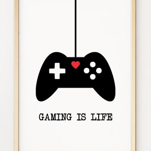 May include: A black and white illustration of a video game controller hanging from a string with a red heart in the centre. The text "GAMING IS LIFE" is below the controller.