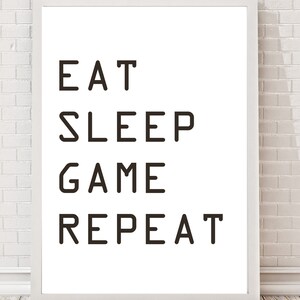 May include: White framed print with black text that reads "Eat Sleep Game Repeat".
