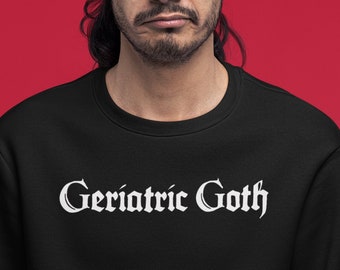 May include: Black crewneck sweatshirt with the text "Geriatric Goth" in a white gothic font. The sweatshirt is worn by a person with dark hair and a red background.