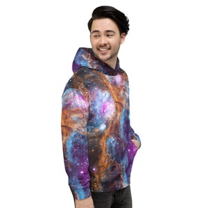 May include: A hooded sweatshirt featuring a vibrant galaxy design in shades of blue, purple, and orange. The pullover has a front pocket and a drawstring hood. The fabric appears soft and comfortable.