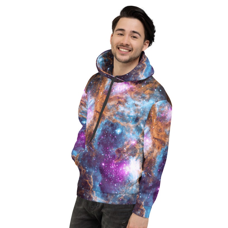 May include: A hooded sweatshirt featuring a vibrant galaxy print in shades of blue, purple, and orange. The hoodie has a drawstring and a front pocket. The overall design creates a cosmic and celestial theme.