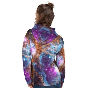May include: A hooded sweatshirt featuring a vibrant galaxy design in shades of blue, purple, and orange. The celestial pattern covers the entire garment, including the hood. The sweatshirt is made of a soft material.