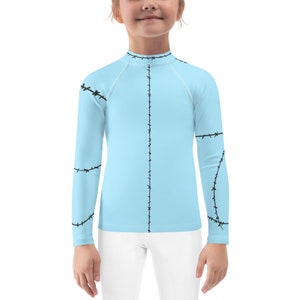 May include: A light blue long-sleeved shirt with black stitching detail. The stitching resembles stitches on a sewn doll.