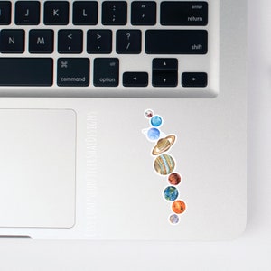 K&ouml;nnte beinhalten: Ein Aufkleber mit den Planeten unseres Sonnensystems in der Reihenfolge von der Sonne aus, mit aquarellartigen Details. Der Aufkleber befindet sich auf einem silbernen Laptop.