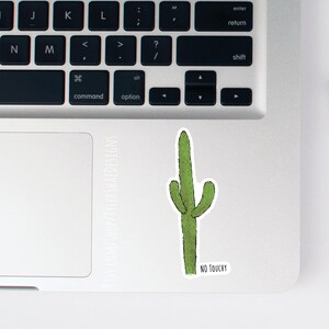 May include: A green cactus sticker with the text "NO TOUCHY" on a silver laptop.