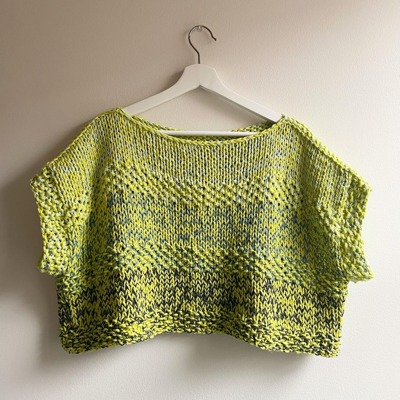 Puede incluir: Un top de punto de manga corta, amarillo y verde, con un patr&oacute;n de chevron. El top es corto y tiene un escote amplio.