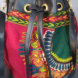 May include: A black leather bucket bag with a drawstring closure and gold metal accents. The bag features a colorful African print fabric lining with a red, green, yellow, and blue pattern.