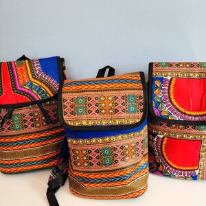 May include: Three colorful backpacks with African print designs. The backpacks are made of fabric and have a drawstring closure. The designs feature geometric patterns in shades of red, blue, yellow, and green.