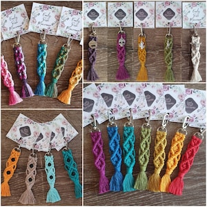 May include: An assortment of colourful macrame keychains with various charms. The keychains are made with a variety of colours, including pink, blue, green, purple, and yellow. Each keychain has a small charm attached to the end, such as a skull, a bear, or a flower.