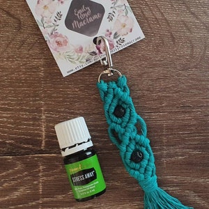 May include: Teal macrame keychain with black beads and a tassel. The keychain has a silver clip and is attached to a small bottle of Young Living Stress Away essential oil.