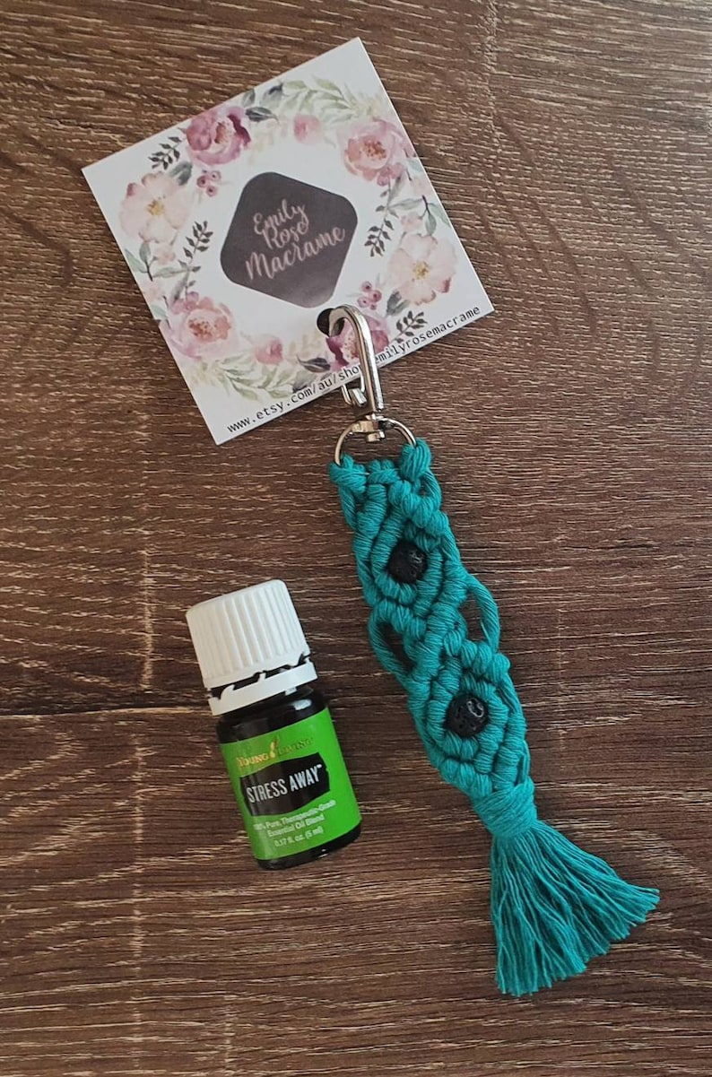 May include: Teal macrame keychain with black beads and a tassel. The keychain has a silver clip and is attached to a small bottle of Young Living Stress Away essential oil.