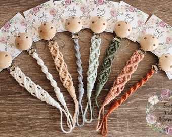 May include: Nine handmade crocheted pacifier clips with wooden beads and clips. The clips are in various colors, including white, beige, gray, green, orange, and brown. Each clip has a tag with the name "Emily Rose" printed on it.