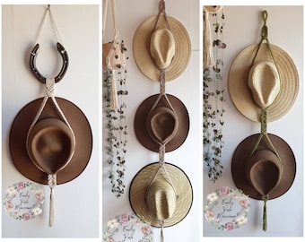 May include: Three macrame hat holders with different colored cords and tassels. Each holder has three hats, one brown felt hat, one straw hat, and one brown felt hat. The holders are hung on a wall with a horseshoe hook.