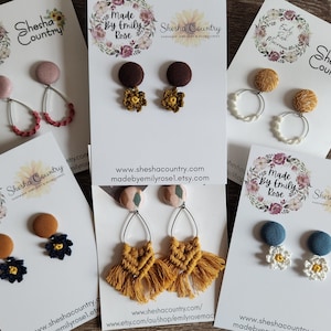May include: A selection of handmade earrings featuring a variety of fabric and crocheted designs. The earrings are displayed on white cards with the text "Shesha Country" and "Made by Emily Rose".