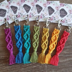 May include: Seven colorful macrame keychains with silver key rings. The keychains are made with a variety of colors, including purple, blue, green, yellow, and red.