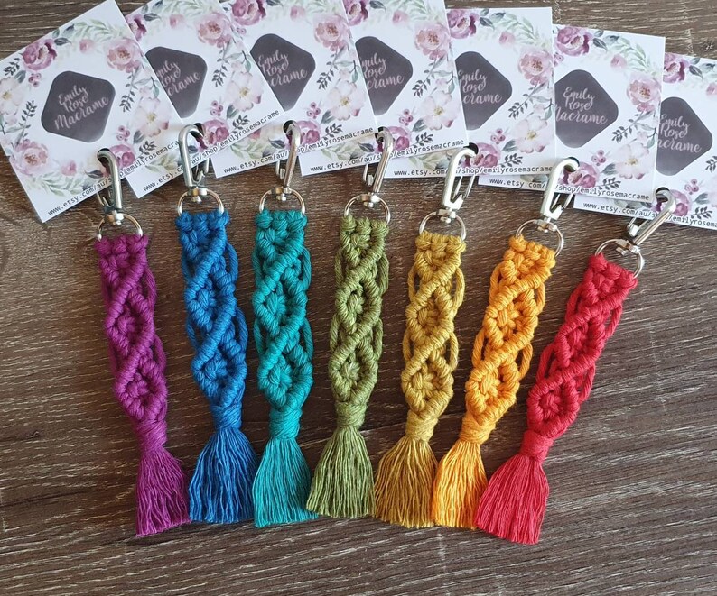 May include: Seven colorful macrame keychains with silver key rings. The keychains are made with a variety of colors, including purple, blue, green, yellow, and red.