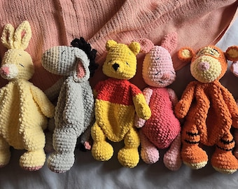 May include: A collection of handmade crochet character dolls, including a bear, rabbit, donkey, Winnie the Pooh, Piglet, Tigger, and an elephant. The dolls are in various colors, with the bear wearing a blue shirt. The image includes a logo that says "Made By Emily Rose."