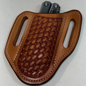 May include: A tan leather belt sheath featuring a basketweave pattern and white stitching. The sheath has two vertical belt slots on the sides and contains a silver metal multi-tool with visible rivets at the top edge of the leather pouch.