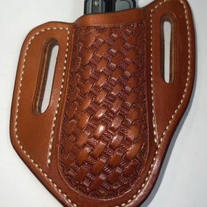 May include: A brown leather multi-tool sheath with a woven basket pattern. The sheath has two slots for a multi-tool and features white stitching around the edges. A silver and black multi-tool is partially visible.