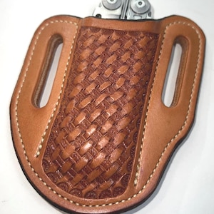 May include: A brown leather multi-tool sheath with a woven pattern on the front. The sheath has two belt loops and white stitching around the edges. A silver multi-tool is partially visible at the top.