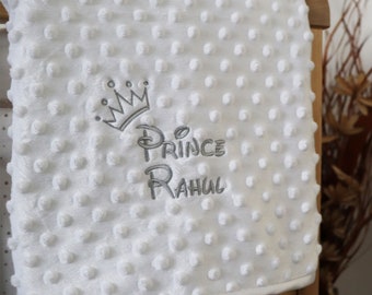 May include: White baby blanket with a gray embroidered crown and the text "Prince Rahul".