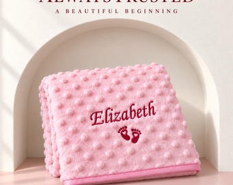 May include: A soft pink baby blanket with a raised dimpled texture. The blanket features the embroidered name Elizabeth in dark pink script, positioned above a pair of small dark pink baby footprints with heart-shaped heels.