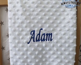 May include: White baby blanket with a textured surface and the name "Adam" embroidered in blue.