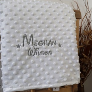 May include: White baby blanket with a gray embroidered name "Meghan Wilson" and two stars.
