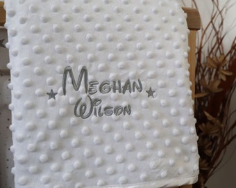 May include: White baby blanket with a gray embroidered name "Meghan Wilson" and two stars.