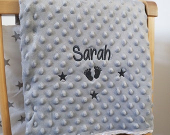 May include: A gray baby blanket with a textured surface. The blanket is embroidered with the name "Sarah", a pair of footprints, and three stars.