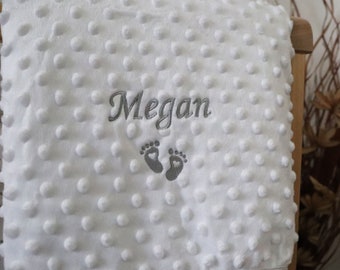 May include: White baby blanket with a gray embroidered name "Megan" and two small footprints.