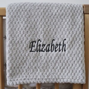 Puede incluir: Una manta de bebé gris texturizada con el nombre "Elizabeth" bordado en negro.