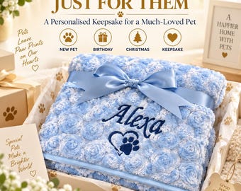 May include: A light blue textured blanket with a rose-like pattern, featuring a dark blue embroidered name Alexa above a heart and paw print design. The blanket is folded and tied with a matching light blue satin ribbon in a bow.