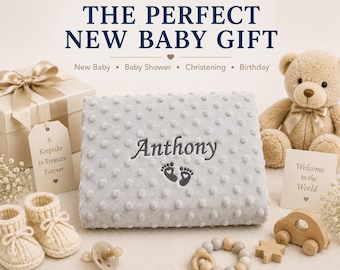 May include: A light gray dimpled baby blanket embroidered with the name Anthony and two small footprints. The blanket is surrounded by a gift box with a ribbon, a beige teddy bear, knitted booties, a pacifier, and wooden baby toys.
