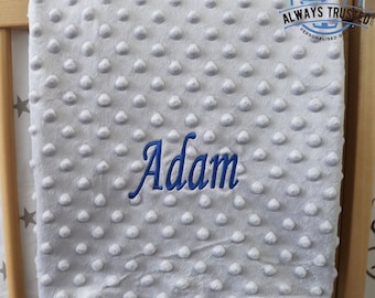 May include: A gray baby blanket with a textured surface and the name "Adam" embroidered in blue.