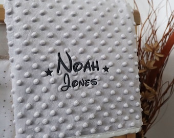 May include: A gray baby blanket with a textured surface and black embroidered stars and the name "Noah Jones".