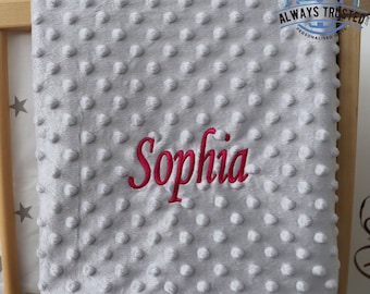 May include: A gray, soft, plush baby blanket with a textured dot pattern. The blanket is personalized with the name "Sophia" embroidered in pink.