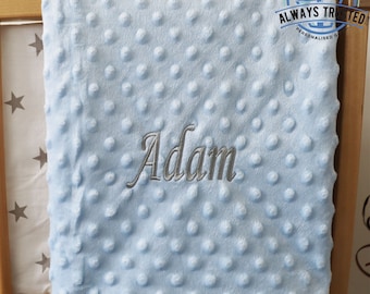 May include: A light blue baby blanket with a textured surface and the name "Adam" embroidered in silver thread.