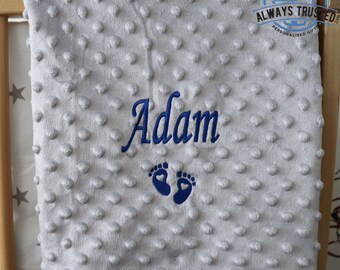 May include: A gray baby blanket with a white border and blue embroidered footprints and the name "Adam".