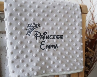 May include: A gray baby blanket with a white polka dot pattern. The blanket has the words "Princess Emma" embroidered on it with a crown above the name.