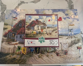 May include: A 300-piece jigsaw puzzle featuring a coastal scene with houses, flags, and kites. The puzzle includes the text "Charles Wysocki" and "Buffalo". The image depicts a beach with a house, boat, and lifeguard stand.