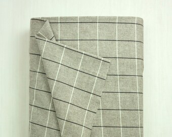 Può includere: Un pezzo di tessuto a quadri grigio e bianco piegato. Il tessuto ha una texture sottile e un aspetto tessuto.