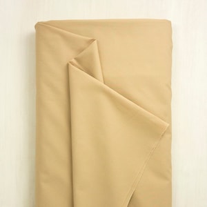 Könnte beinhalten: Ein gefaltetes Stück beigefarbenes Stoff. Der Stoff ist glatt und hat einen dezenten Glanz.