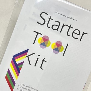 May include: A white card with the text "Starter Tool Kit" in black and colorful geometric shapes. The card lists 10 items included in the kit, including a 15 cm ruler, silk pins, needles, a seam ripper, an erasable pen, a needle threader, embroidery scissors, a silicone thimble, and fabric clips.