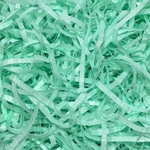 May include: A close-up of a pile of light green shredded paper, commonly used as packing material or for gift wrapping.