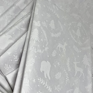 May include: A stack of white tissue paper with a subtle embossed pattern of woodland animals, trees, and stars. The pattern is in a light gray color.
