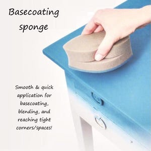 May include: A beige basecoating sponge for applying paint to surfaces. The sponge is shaped like a rounded rectangle and is being held by a hand. The text "Basecoating sponge" is written in black above the sponge. The text "Smooth & quick application for basecoating, blending, and reaching tight corners/spaces!" is written in black below the sponge.