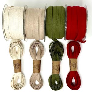 May include: An assortment of spools and bundles of cotton twill ribbon in various colors. The colors include cream, beige, olive green, and red. The ribbon is available on spools and in bundles with paper labels.
