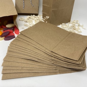 May include: A stack of twenty-five brown paper bags, folded and ready to use. The bags are made of a sturdy, kraft paper and are perfect for packaging small gifts or favors.